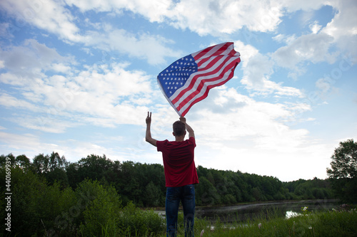 A young man waves a US flag in the open air. View from the back.