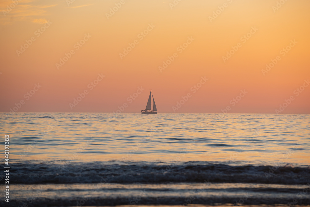 Sailing yacht on sunrise over the sea and beautiful cloudscape. Colorful ocean beach sunset.