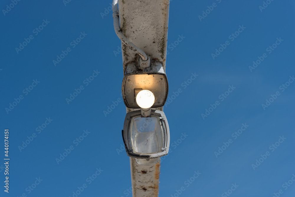 Fototapeta premium old walkway lamp with diffuser glass cover hanging down and illuminated LED bulb against a blue sky
