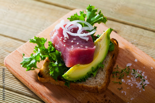 Delicious sandwich with avocado slice, raw tuna fillet and fresh greens garnished with sesame