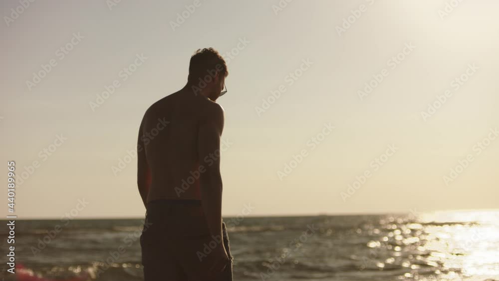 Low angle back view shot topless man walking on beach in late afternoon sun. Summer at seaside. Low angle back view shot topless man walking on beach in late afternoon sun. Summer at seaside.