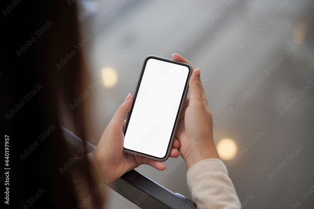 Backside view of woman hand using mockup white screen mobile phone.