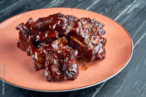 Appetizing and juicy beef ribs in barbecue sauce, served in a plate on a dark background. American BBQ culture