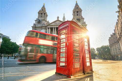 Red Telephone booth at sunrise with blurry bus passing by near St Pauls Cathedral in London
