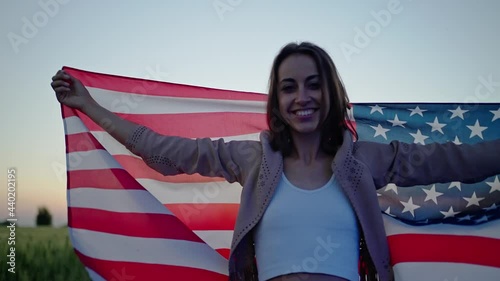 cheerful young woman wrapped in United States flag outdoors with polica lights on face. photo