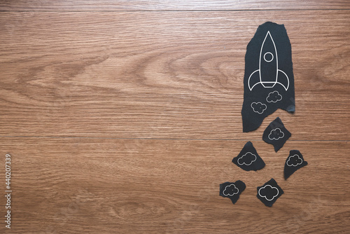 A piece of paper with rocket icon and smoke on wooden background with copy space.
