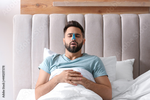 Foto Man with clothespin suffering from runny nose in bed