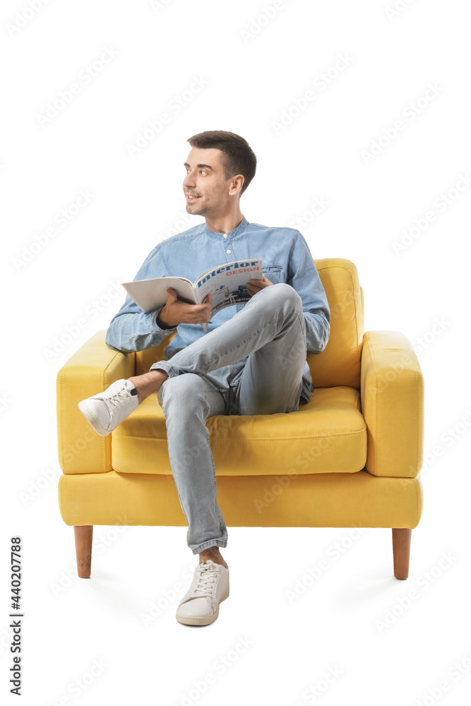 Young man with magazine sitting in armchair on white background