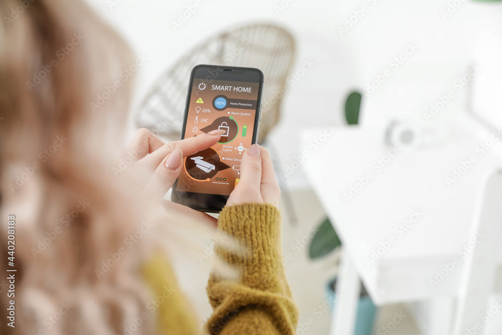 Woman with mobile phone using smart home security system application Woman with mobile phone using smart home security system application