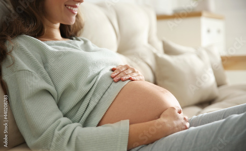 Pregnant woman touching her belly indoors, closeup