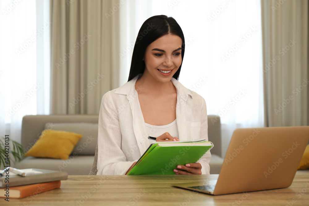 Young woman taking notes during online webinar at table indoors Young woman taking notes during online webinar at table indoors