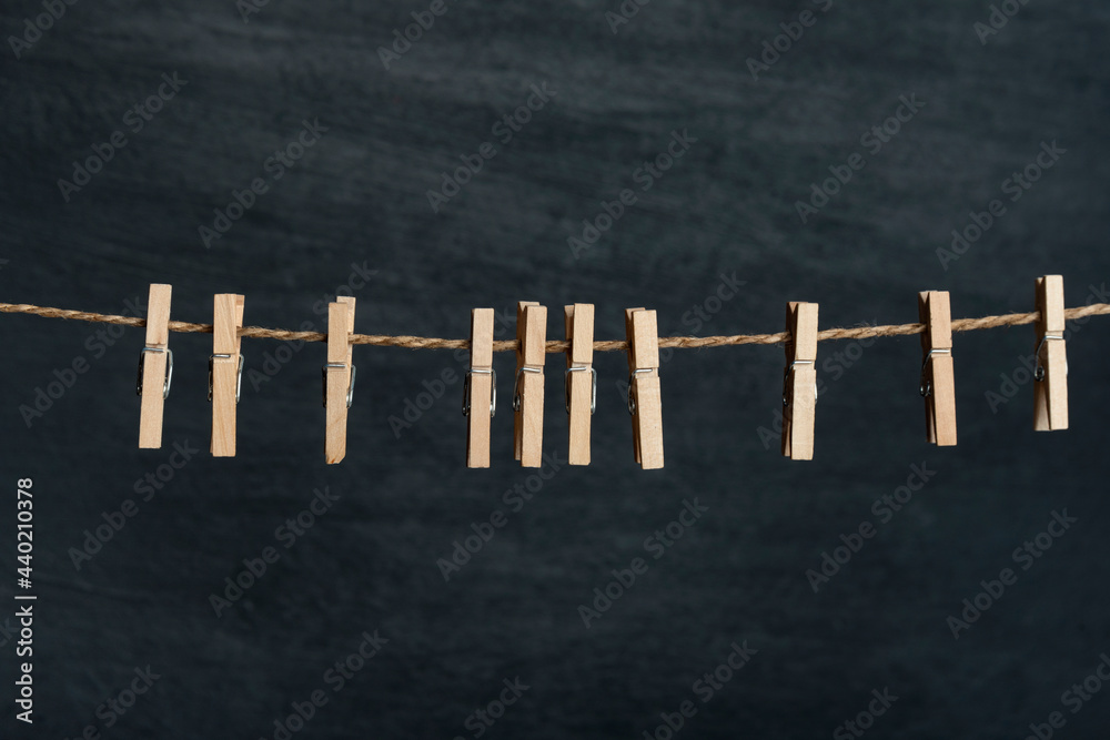 Fototapeta premium Several wooden cloth clips in rope waiting for clothes to come after laundry. Black wall on the background