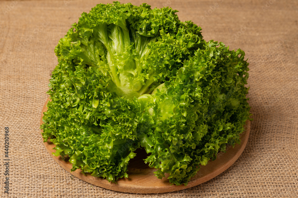 three bunches of lettuce lies on a round wooden board, against a background of linen fabric, close-up
