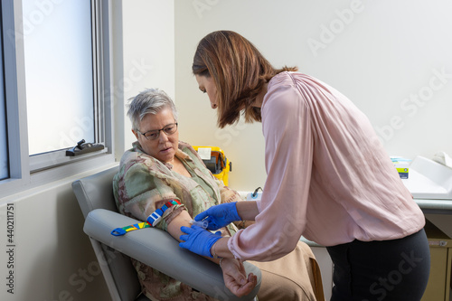 mature woman in phlebotomy chair with nurse taking blood test