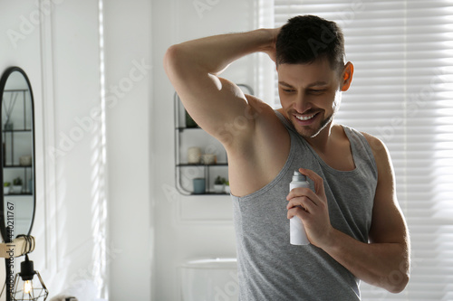 Handsome man applying deodorant in bathroom. Space for text photo