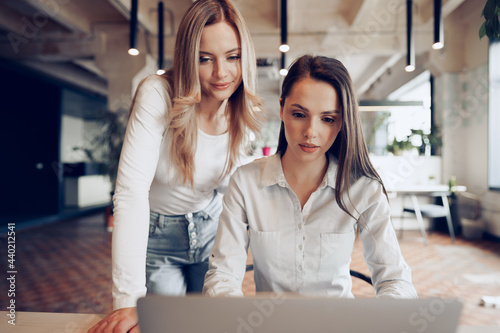 Two young female colleagues discussing business project together in office