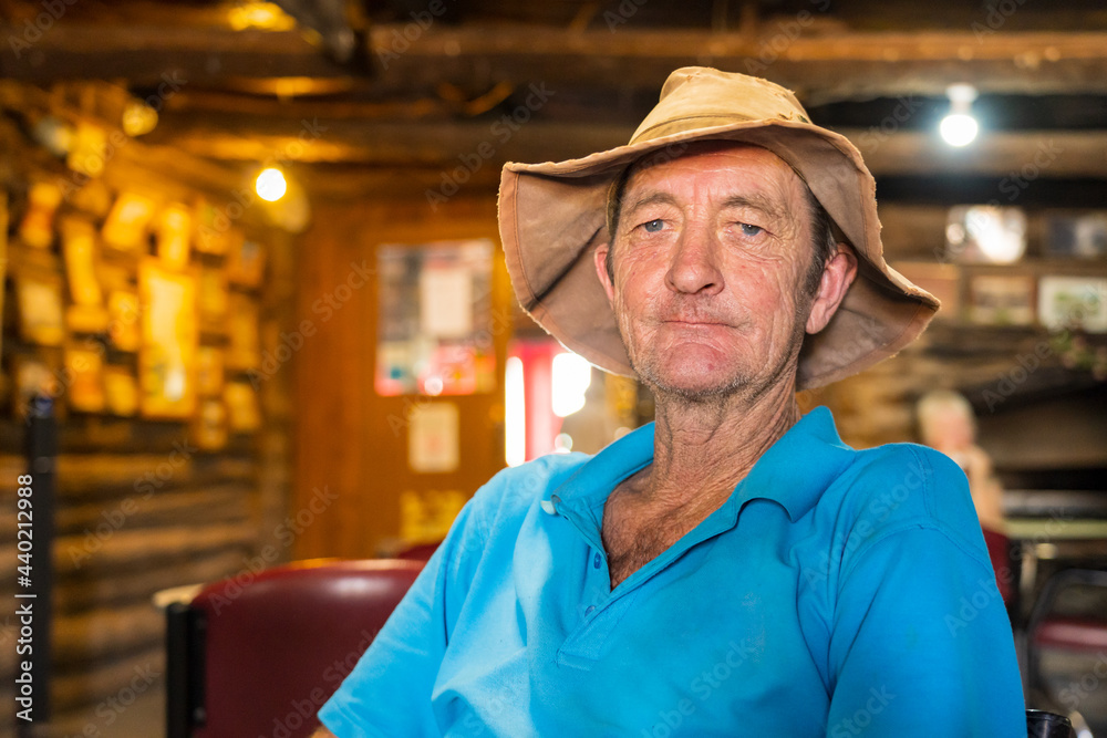 An elderly man in an outback pub wearing a floppy hat and smiling