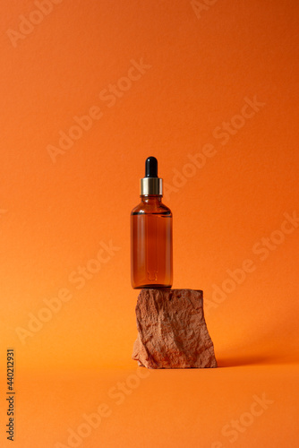 Amber glass dropper bottle with metallic lid on a piece of stone. Orange background with daylight. Skincare products , natural cosmetic. Beauty concept for face and body care