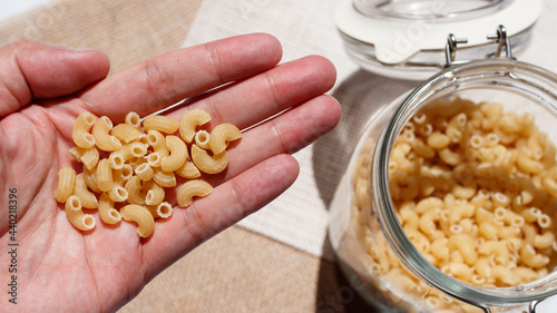 Focus on the uncooked macaronies in the male's hand and the blurred macaroni's bottle on the right side
