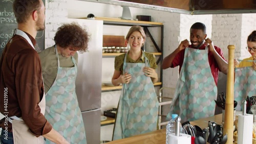 Group of cheerful multiethnic men and women smiling and chatting with chef while putting on aprons before culinary master class photo