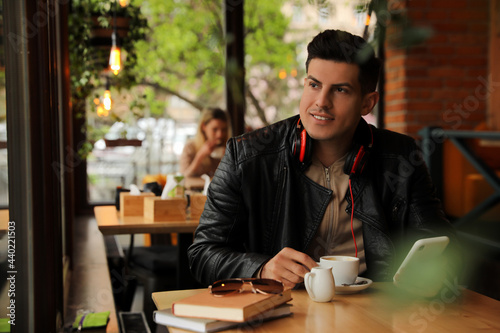 Man with headphones and smartphone at table in cafe