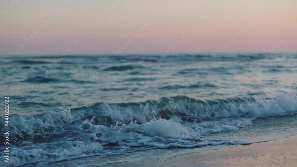 Close-up view of rolling waves on sandy beach at sea coast. Pink twilight sky. Summer evening at seaside. Close-up view of rolling waves on sandy beach at sea coast. Pink twilight sky. Summer evening at seaside.