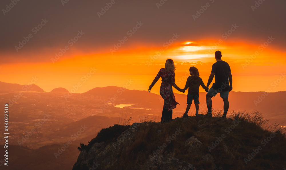Mother and father next to her son looking at the horizon in a beautiful sunset on the mountain. Adventure lifestyle A summer afternoon in the mountains of the Basque country