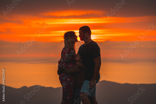 Parents on the top of a mountain at sunset and his son watching them, kisses and family love. Adventure lifestyle A summer afternoon in the mountains of the Basque country