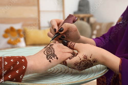 Professional mehndi master making henna tattoo indoors, closeup photo