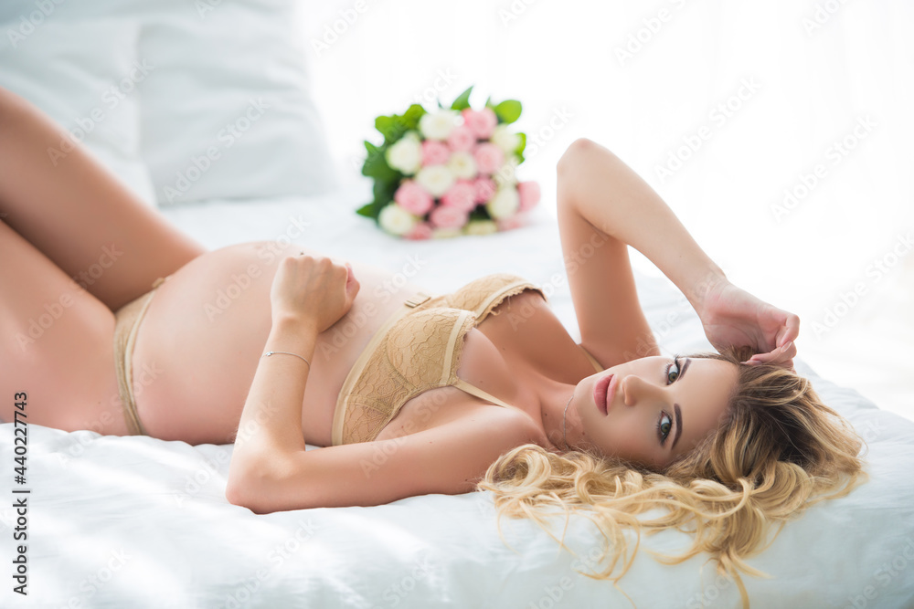 Obraz premium Beautiful blonde woman lies in lingerie on the bed with a bouquet of roses flowers. Delicate scent and femininity