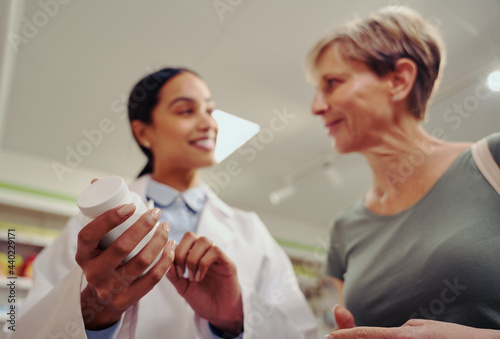 Closeup of young pharmacist hand holding and checking medicine dosage and ingredients with expiry date standing near shelf in chemist shop with senior woman