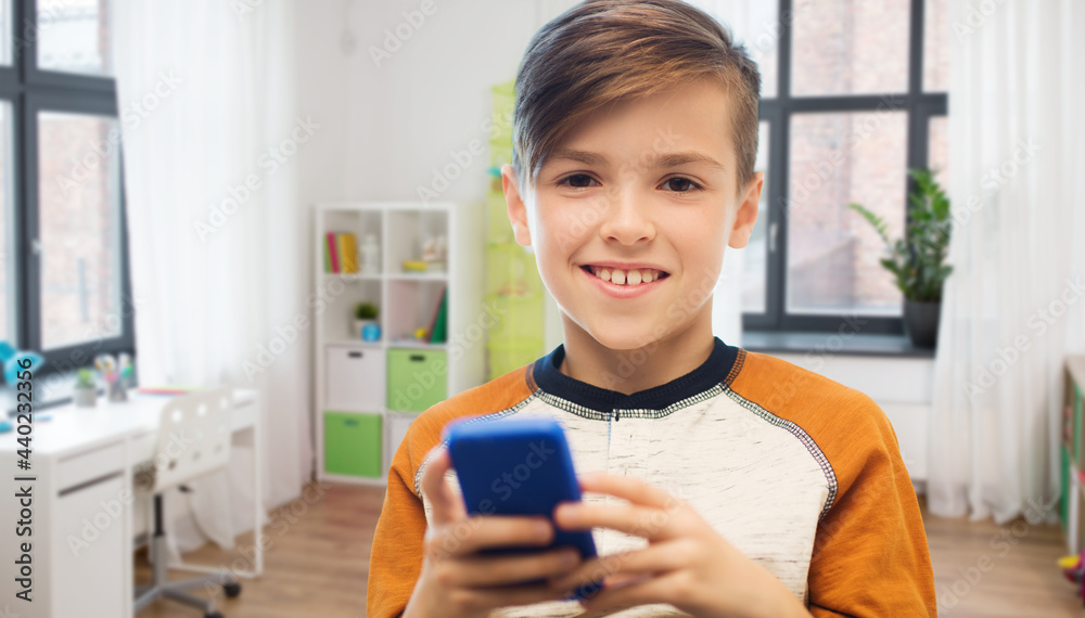 leisure, children, technology, internet communication and people concept - smiling boy with smartphone texting message or playing game at home over children's room background leisure, children, technology, internet communication and people concept - smiling boy with smartphone texting message or playing game at home over children's room background