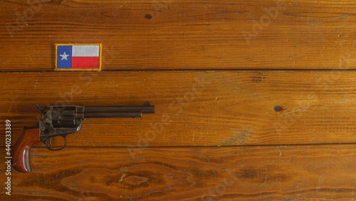 Single action revolver below a Texas state flag patch on a textured wooden plank background