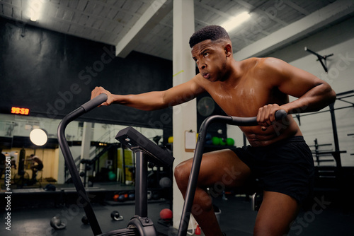 African American male using an elliptical trainer during cross fit training. Male athlete exercising intensely in the gym. High quality photo © StratfordProductions