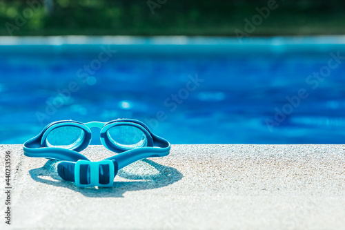 Blue swimming goggles on stone curb of swimming pool with blue water in background