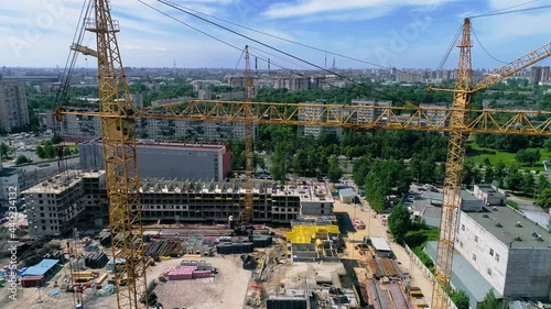 Fly around tower cranes at a construction site on a clear summer day. Yellow cranes with a hoist rope or wire ropes. Mast, slewing unit, operating cabin, main jib are visible.