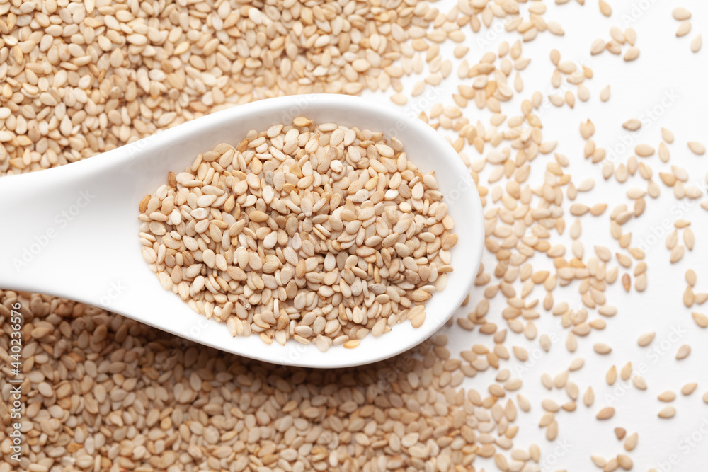 Macro Close up of Organic White Sesame seeds(Sesamum indicum) or white Til with shell on a white ceramic soup spoon. Top view, over gradient background of itself. Macro Close up of Organic White Sesame seeds(Sesamum indicum) or white Til with shell on a white ceramic soup spoon. Top view, over gradient background of itself.