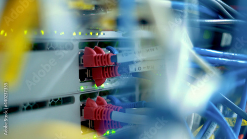 Close up network cables attached to cloud computing system with blinking lights in server room.