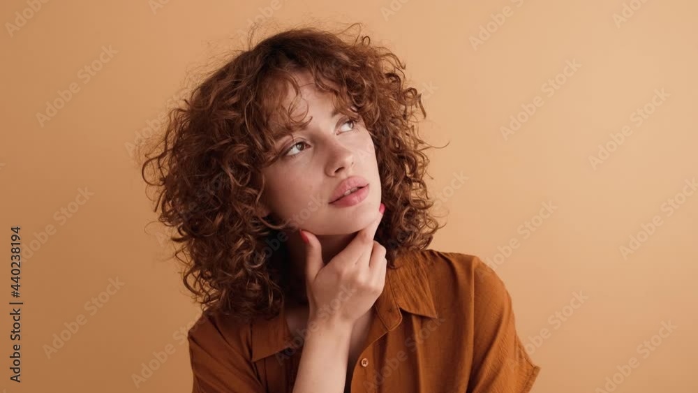 A close-up view of a pleased woman is dreaming about something standing isolated over a beige wall in the studio A close-up view of a pleased woman is dreaming about something standing isolated over a beige wall in the studio