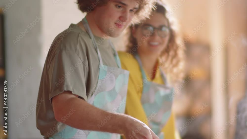 Young Caucasian man in apron tossing vegetables on frying pan while learning how to cook during culinary class