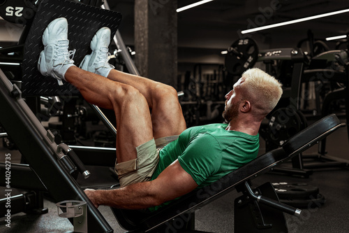 Bild auf Leinwand Inflated young athlete doing leg exercises in the gym, swinging legs, muscle mas