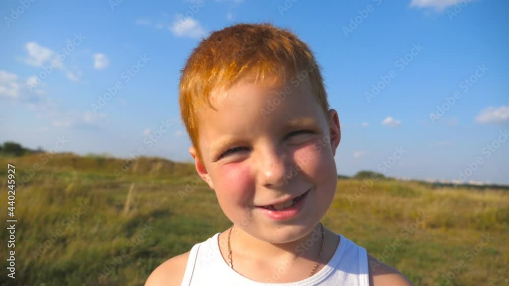 Portrait of happy red hair boy with freckles laughs outdoor. Adorable handsome baby looking into camera with joyful smile. Close up emotions of male child with glad expression on face. Slow motion Portrait of happy red hair boy with freckles laughs outdoor. Adorable handsome baby looking into camera with joyful smile. Close up emotions of male child with glad expression on face. Slow motion