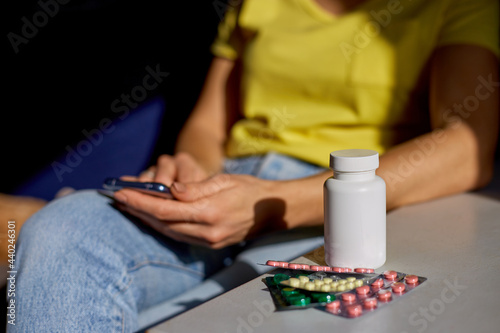 Unrecognizable woman sitting on sofa with blister pack of pills using online pharmacy store