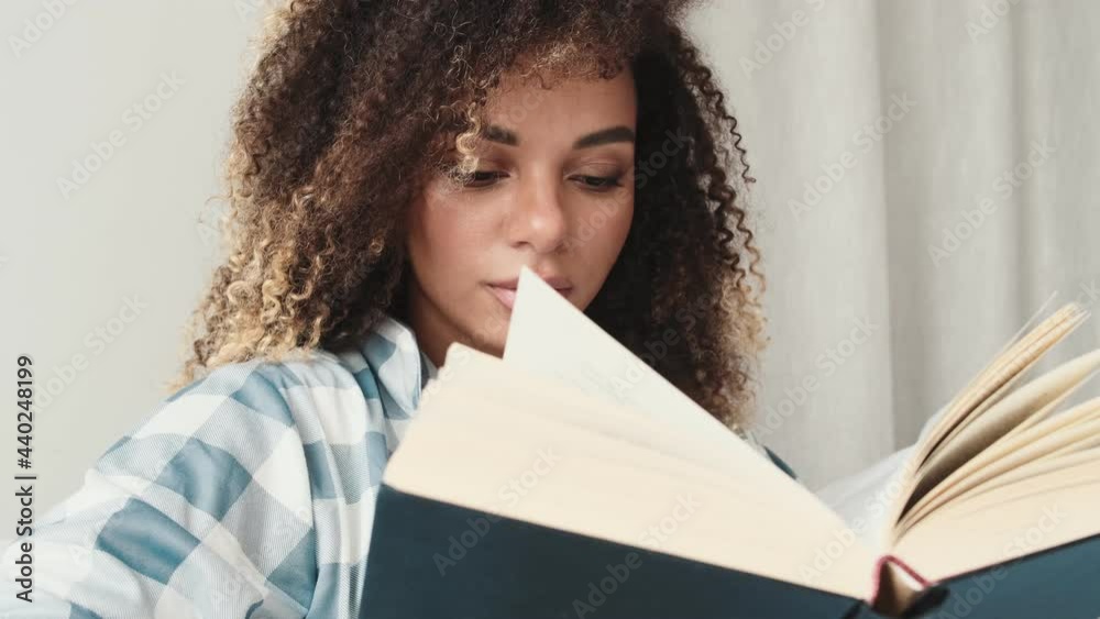An attractive african american woman wearing pajama is reading a book sitting on the sofa at home An attractive african american woman wearing pajama is reading a book sitting on the sofa at home