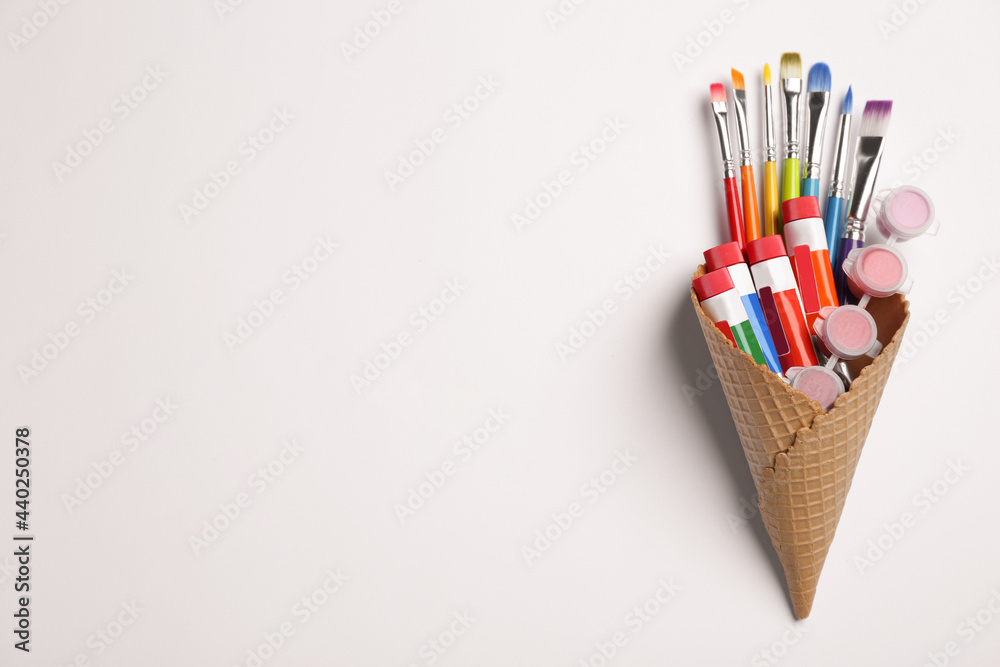 Waffle cone with different paints and brushes on white background, top view. Space for text Waffle cone with different paints and brushes on white background, top view. Space for text