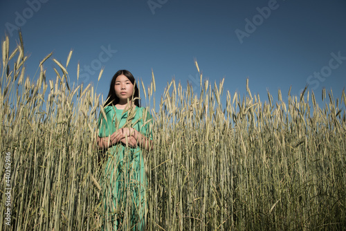 asian girl in green dress standing in the middel of a wheat grain field under blue sky in summer photo