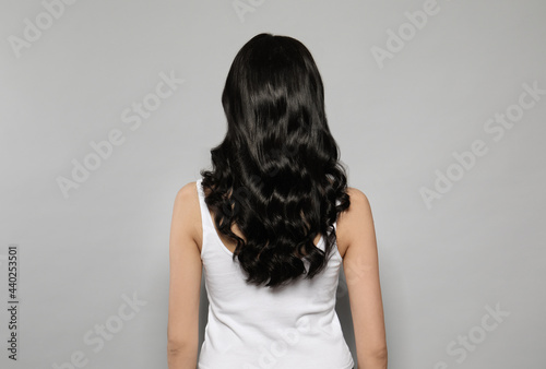 Young woman with long curly hair on grey background, back view