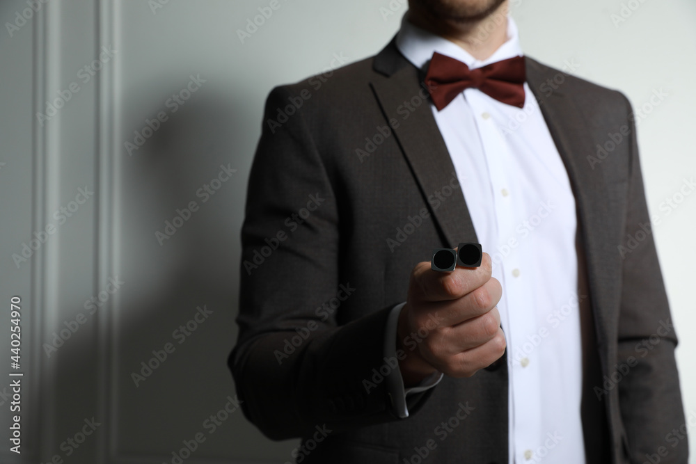 Man in suit holding stylish cufflinks near white wall, closeup. Space for text Man in suit holding stylish cufflinks near white wall, closeup. Space for text