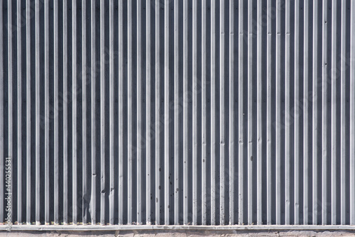 Metallic industrial background with pinstripes. The metal cover is painted with gray paint. Metal fence, strip, line, corrugated sheet, corrugated metal