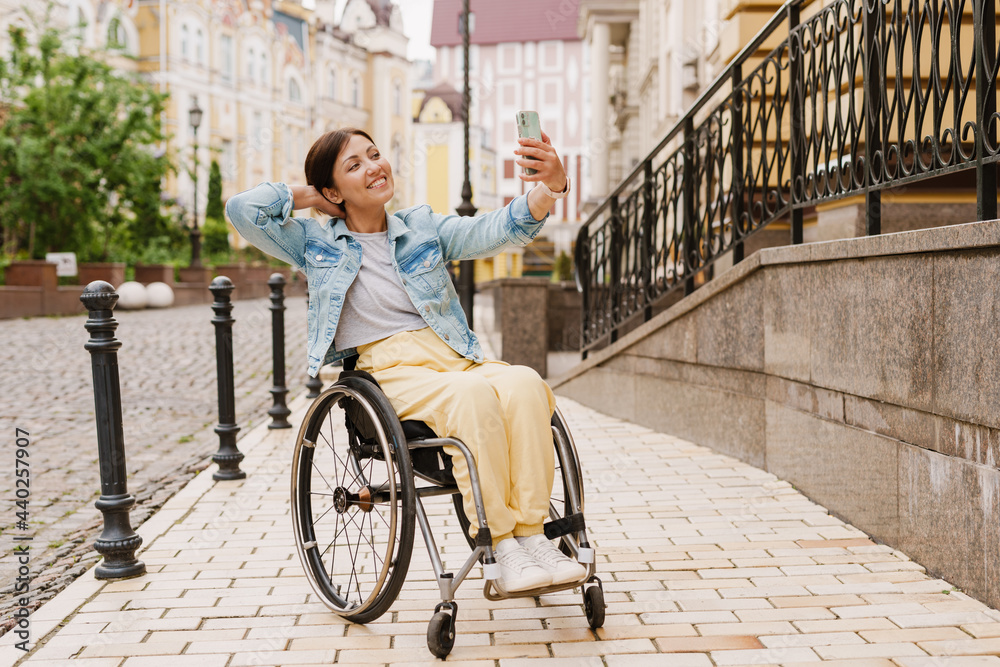 Brunette woman taking selfie on mobile phone while sitting in wheelchair